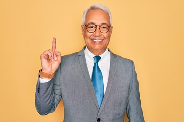 Poster - Middle age senior grey-haired handsome business man wearing glasses over yellow background showing and pointing up with finger number one while smiling confident and happy.