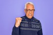 © Krakenimages.com - Middle age senior grey-haired man wearing glasses and winter sweater over purple background angry and mad raising fist frustrated and furious while shouting with anger. Rage and aggressive concept.