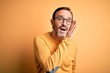 © Krakenimages.com - Middle age hoary man wearing casual sweater and glasses over isolated yellow background hand on mouth telling secret rumor, whispering malicious talk conversation