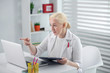 © zinkevych - Serious woman in a medical coat chatting online.