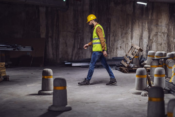 Wall Mural - Young attractive bearded worker in west with helmet on head walking around in tunnel in construction process.