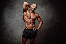 Sportive Adult Male Wearing Sportswear Posing While Showing His Muscles, Smiling And Looking At The Camera In A Dark Studio