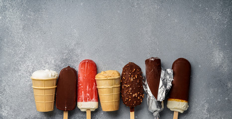 Poster - Chocolate ice cream popsicles and fruit ice cream with cones on gray cold stone background. Copy space for text.