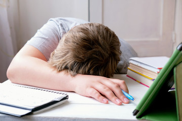 tired boy laying on the table top. Learning and exam concept. boy with pc tablet and schoolbooks falls asleep. upset with homework pupil.