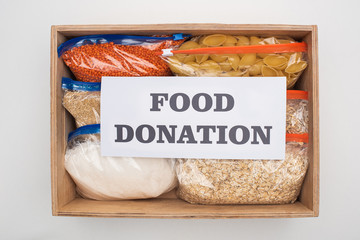 Wall Mural - top view of pasta and groats in zipper bags in wooden box with food donation card on white background