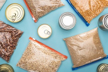 Wall Mural - top view of cans and groats in zipper bags on blue background, food donation concept