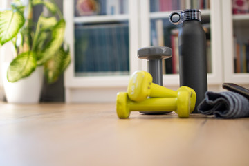 Fitness at home, equipment and tools for gym at home. Dumbbell with towel, mobile phone and water, protein bottle on wooden parquet floor. Background copyspace sport activity at home with accessories.