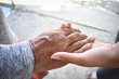 © aekkawin - Hands of two people represent family warmth and care for the elderly.