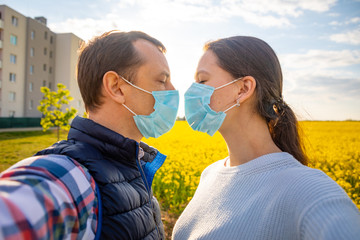 man and woman kissing each other in protective medical mask on face in countryside