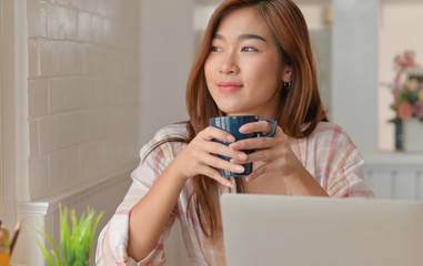 Teenage student smile and drink coffee while studying online from their home laptop.