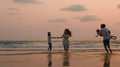 © tirachard - Asian young happy family enjoy vacation on beach in the evening. Dad, mom and kid relax playing together near sea when silhouette sunset. Lifestyle travel holiday vacation summer concept.