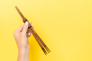 Wall Mural - Female hand holding chopsticks on yellow background. Sushi concept with empty space for your idea