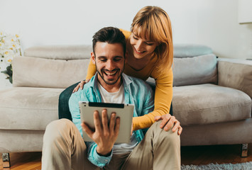 Young couple spending time together at home. Man and woman sitting on the couch and having fun. Watching contents on the tablet