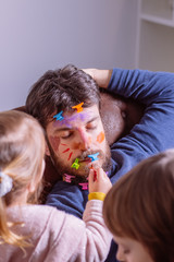 Young father sleeping on the sofa while children paint his face