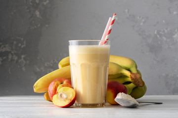 Wall Mural - Fresh protein shake with nectarine or peach on a white wooden table. Fresh apricot milkshake. A glass of banana smoothie.