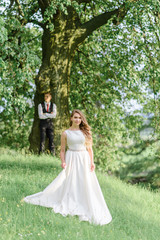  The bride and groom are hugging on the background of a green park. focus on the bride in the foreground.