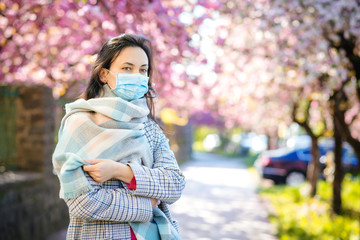 Young woman with face mask in the spring street. Covid-19 world pandemic. Coronavirus outbreak.