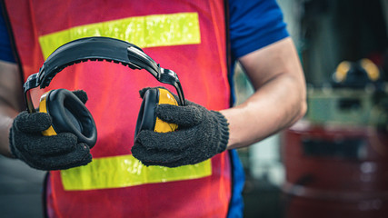 Industrial worker holding ear protection gear equipment.