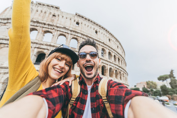 Happy couple of tourist having fun taking a selfie in front of Colosseum in Rome. People travel Rome, Italy.