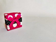 Close-up Of A Bright Pink Gift Box White Polka-dot With A Scarlet Ribbon On A White Texture Background. Space For Your Text. 
Image With Selective Focus And Noise Effects.
