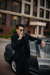 © Andrii - A stylish businessman smokes cigars near a luxury car. Fashion and business