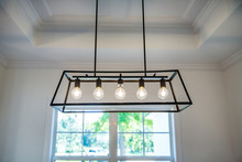 Hanging Retro Black Metal Iron Chandelier Lighting Fixture With Vintage Bulbs Hanging In A Dining Room Of A New Construction House