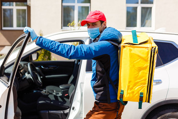 food delivery man in a protective mask and gloves with a thermo backpack near a car during the quarantine period