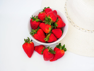 bowl of fresh strawberries with sun hat on white