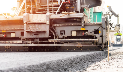 Paver machine is laying fresh asphalt on city road