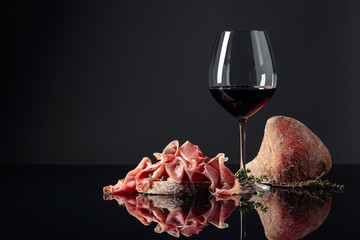 Wall Mural - Prosciutto with bread, red wine and thyme on a black reflective background.