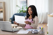 © Syda Productions - remote job, technology and people concept - happy smiling african american young woman with laptop computer and papers working at home office