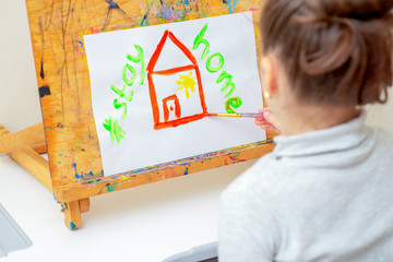 Wall Mural - Child is drawing red house with words Stay Home on white sheet of paper at home. Stay Home concept.