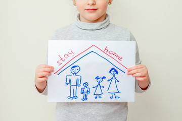 Poster - Little girl is holding a picture of family silhouette under the roof and words Stay Home on yellow background. Children in quarantine concept.