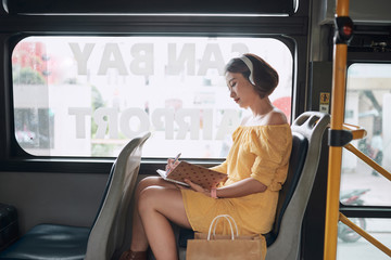 Wall Mural - Beautiful young woman sitting in city bus and writing some notes in notebook.