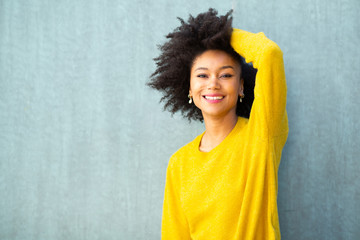 Wall Mural - smiling young black woman posing with hand in hair by green background