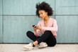 © mimagephotos - young african american woman sitting on floor outside looking at  mobile phone
