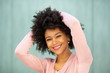 © mimagephotos - Close up smiling young black woman with hands behind head by green background