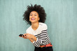 © mimagephotos - smiling young african american woman holding phone by green background