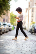 © mimagephotos - Full length young african american woman walking on street looking at mobile phone