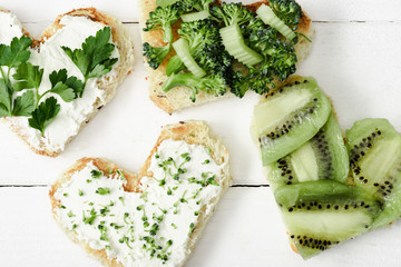 Canvas Print - top view of heart shaped canape with creamy cheese, broccoli, microgreen, parsley and kiwi on white wooden surface