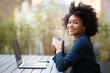 © mimagephotos - smiling young african american business woman sitting with laptop and cup of coffee