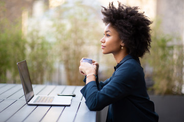 Side of young african american business woman sitting with laptop and cup of coffee