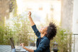© mimagephotos - happy young african american business woman sitting with laptop and hand raised