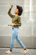 © mimagephotos - Full length cheerful young black woman walking with mobile phone and earphones