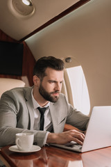 Wall Mural - concentrated businessman typing on laptop near cup of coffee in private plane