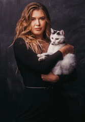 Beautiful young woman holding cat on dark background