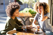 © mimagephotos - happy young african american women sitting at outdoor cafe with cellphone