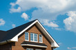 © ilyaska - Metal tile roof of brick house against blue sky with clouds