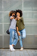 © mimagephotos - Full body two happy young black women taking selfie with cellphones