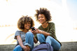 © mimagephotos - two young african american women sitting on steps outside looking at cellphone